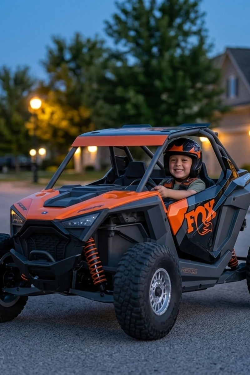 Child sitting in an orange and black off-road vehicle with 'FOX' branding at dusk.